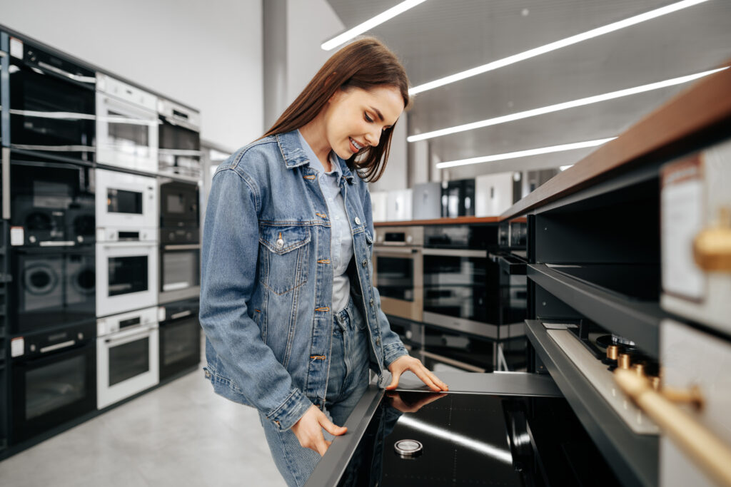 young brunette woman choosing new electric stove in a hypermarket